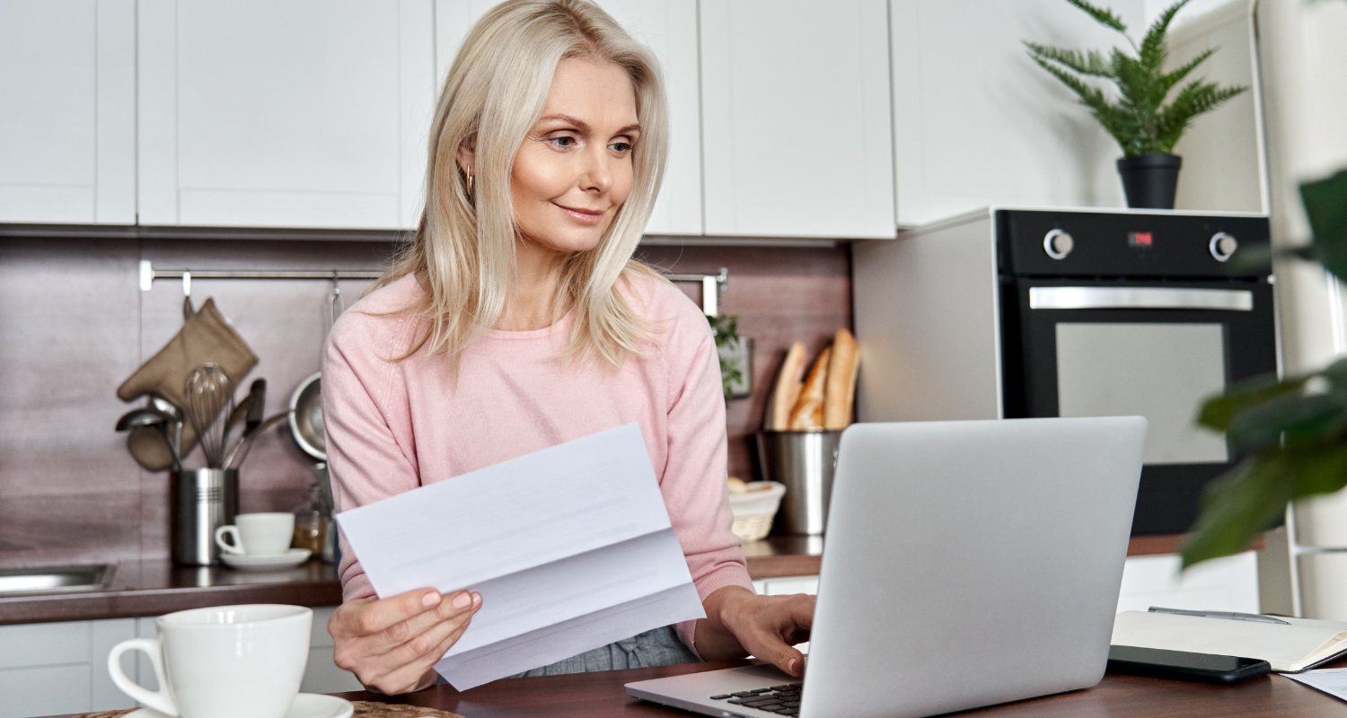 Woman holding paper and looking at laptop